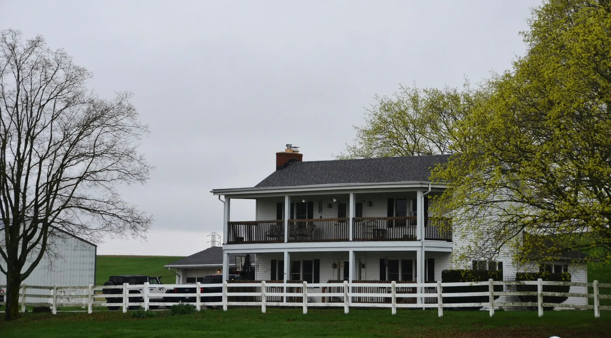 White house with double porches and a shingle roof behind a rail fence